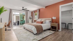 Una camera da letto moderna con un letto grande, una ventola a soffitto, un comodino e vista su un'area pranzo.