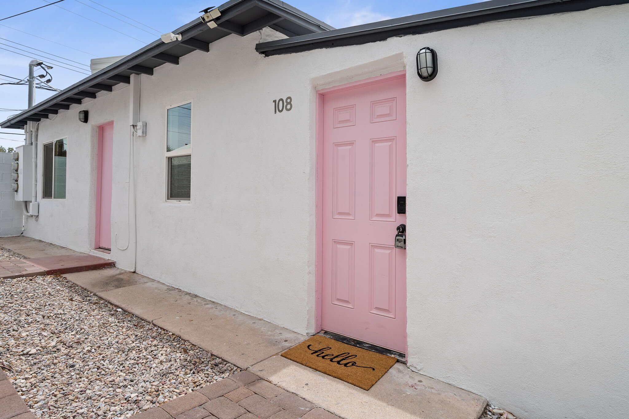 A building with a white exterior, numbered 108, featuring a pink door and a doormat with 'hello' written on it.