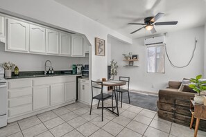 Una cocina moderna con gabinetes blancos, una barra de café y un comedor con mesa y sillas.