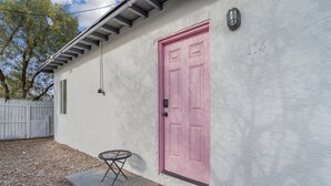 A house with a pink door, a small round table, and a welcome mat. - Casita Rosa - Cozy - Midtown Gem (Tucson)