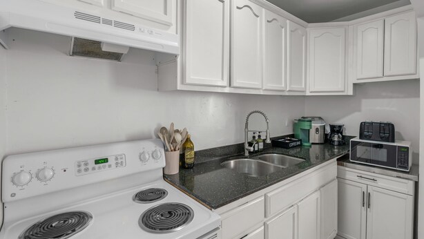 A kitchen with white cabinets, a stove, a sink, and a microwave. - Casita Rosa - Cozy - Midtown Gem (Tucson)