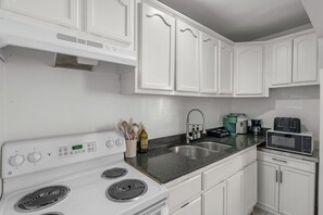 A kitchen with white cabinets, a stove, a sink, and a microwave. - Casita Rosa - Cozy - Midtown Gem (Tucson)