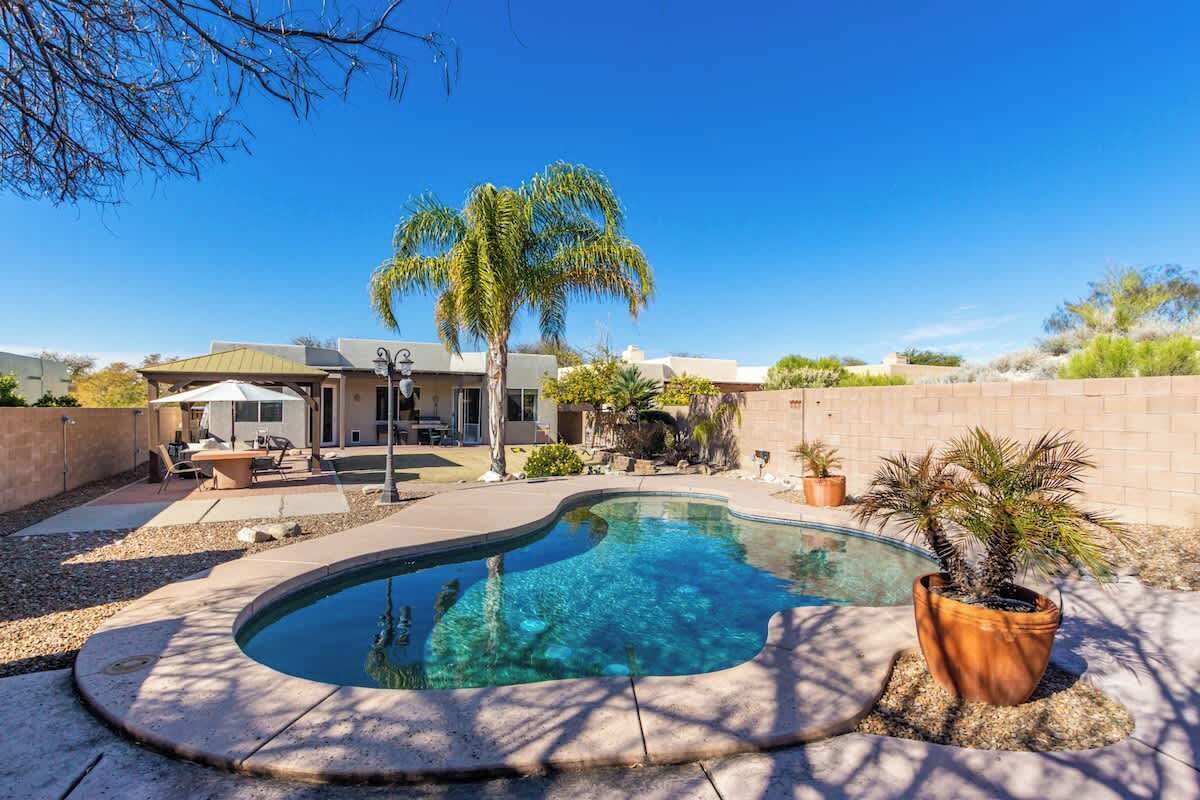 Ein Pool mit geschwungener Kante, umgeben von einer Terrasse mit Gartenmöbeln.