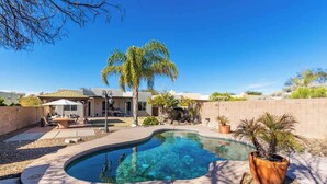 Una piscina de borde curvo, rodeada por un patio con mobiliario exterior.