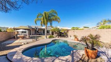 Ein Pool mit geschwungener Kante, umgeben von einer Terrasse mit Gartenmöbeln.