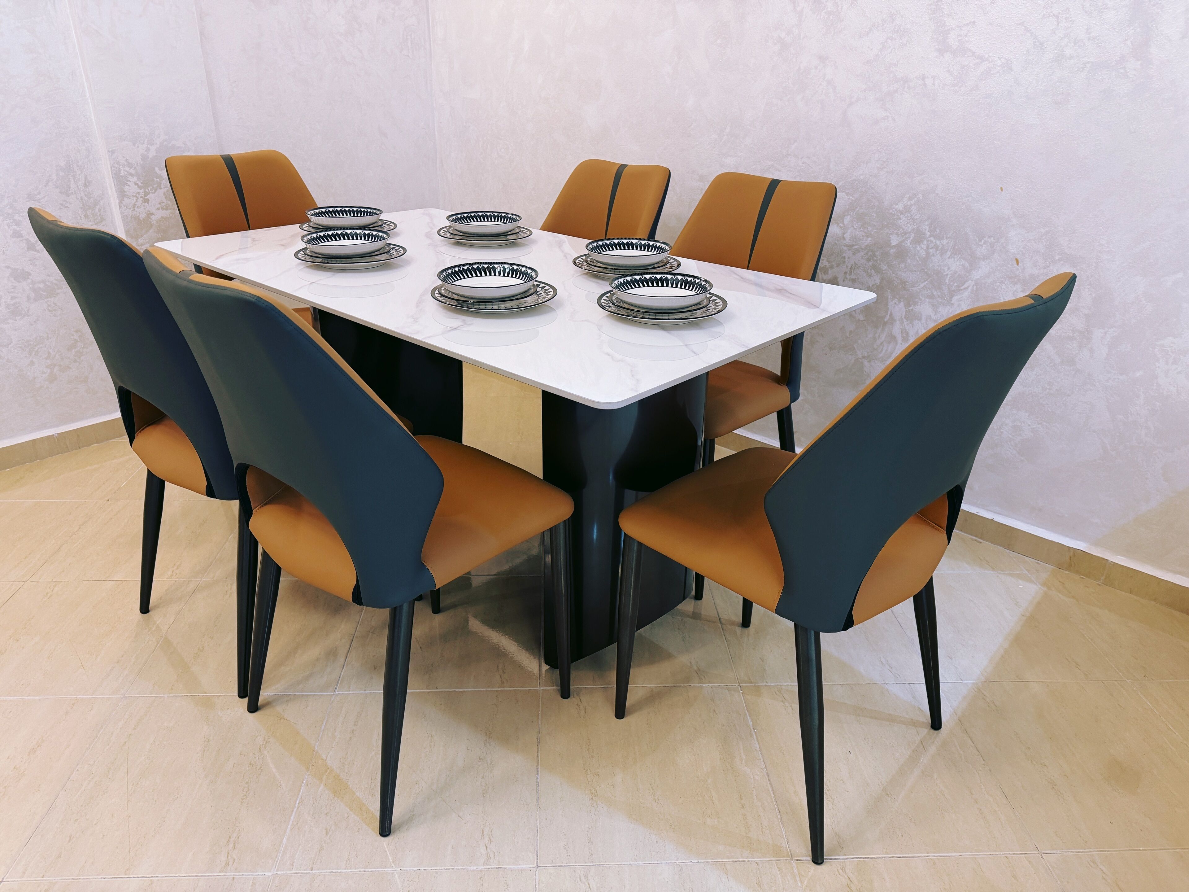 A dining table with six chairs, each with a black and orange design, set against a white marble table.