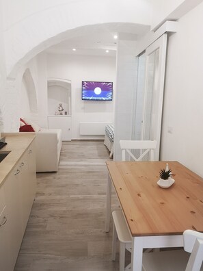 Een moderne keuken met witte kastjes, een houten eettafel en een kleine potplant.