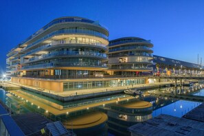 Un hôtel moderne doté de nombreux balcons, offrant une vue sur le front de mer et dont l’image se reflète dans l’eau.