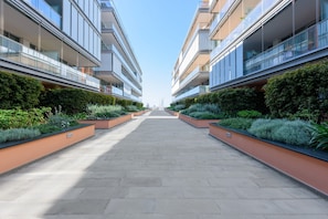 Un bâtiment moderne doté d’une allée centrale bordée de jardinières et de balcons en verre.