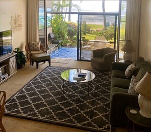 A living room with a large window, a sofa, a coffee table, and a TV. - Walk out to a secluded beach, sea turtles and Maui sunsets - Oceanfront condo (Lahaina)