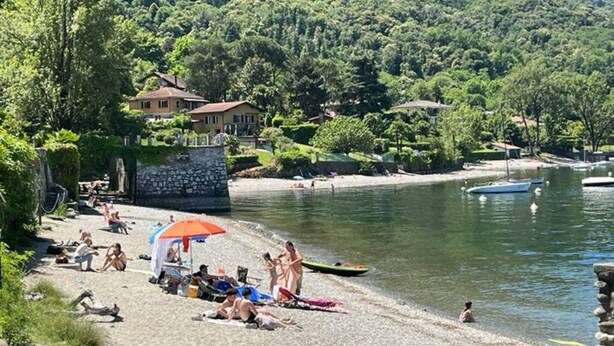 Una playa con gente tomando el sol, un pequeño bote y un muro de piedra.