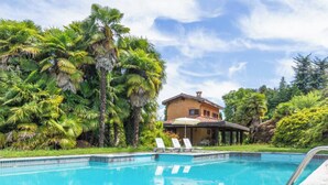 Una piscina con sillones de descanso, rodeada de abundante vegetación y una casa.