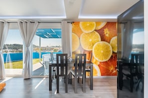 A dining area with a table and chairs, a view through large windows, and a wall with a fruit pattern. - Apartment 'Gr House Eleftheria' with Sea View, Wi-Fi and Air Conditioning (Rhodes)