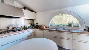 A modern kitchen with a large window, white cabinetry, and a round dining table. - Villa Citriodora  Cernobbio (Cernobbio)