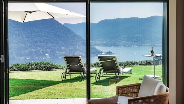 A room with a large glass door leading to a balcony with two lawn chairs and a table with a bottle and glass. - Villa Citriodora  Cernobbio (Cernobbio)