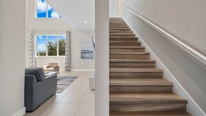 Ein modernes Interieur mit Treppe, einem grauen Sofa und einem großen Fenster mit Blick auf Bäume und Himmel.