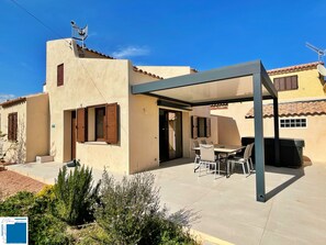 A covered patio area with a table and chairs, a grill, and a satellite dish on the building. - AIR-CONDITIONED VILLA IN SOUTHERN CORSICA: Sleeps 8, 4 Bedrooms, 150 meters from the beach (LECCI)