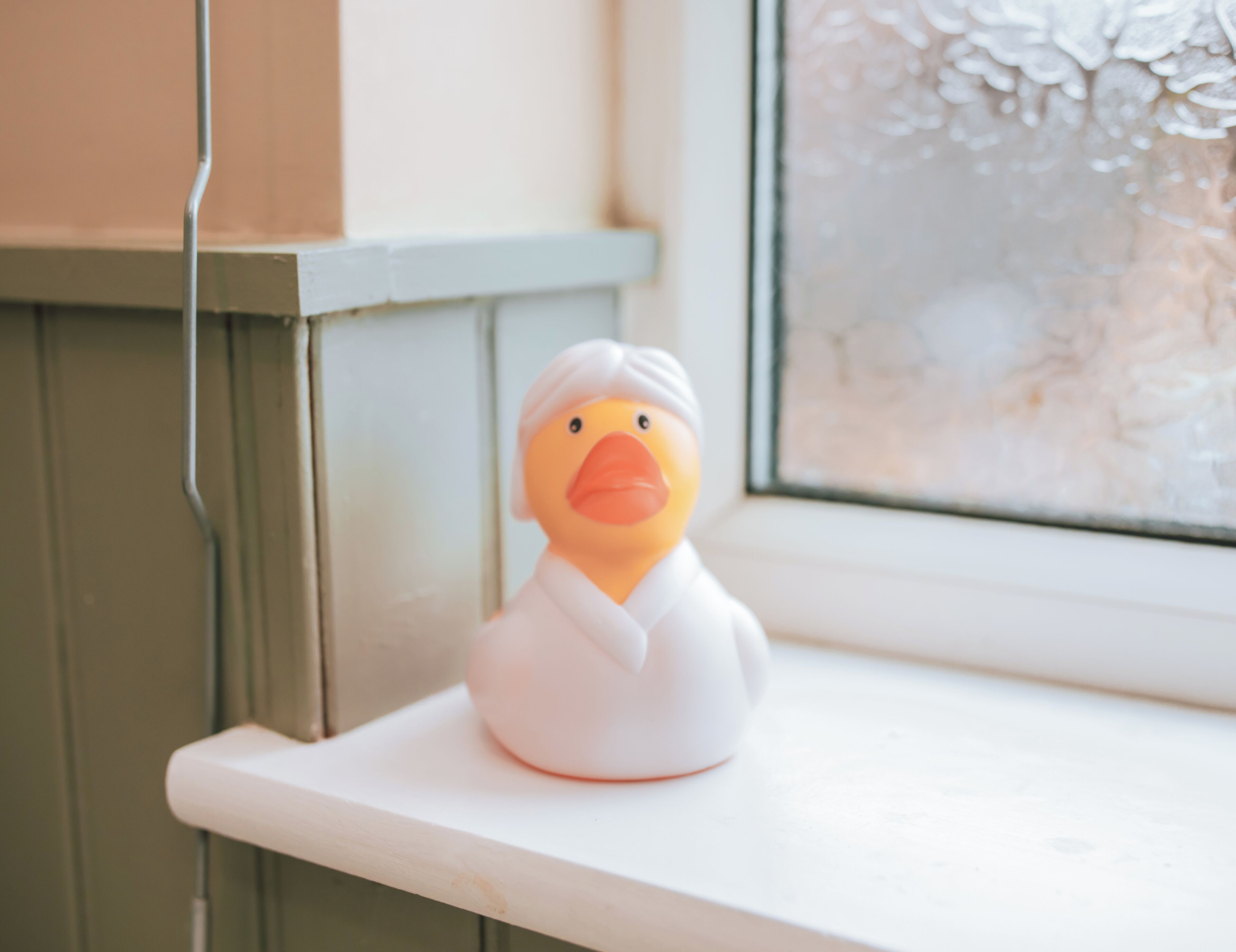 A duck figurine on a white shelf by a window with frosted glass.