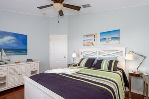 Een slaapkamer met een bed, een plafondventilator, een nachtkastje, een lamp en kunst aan de muur.