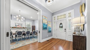 A dining area with a wooden table and chairs, a chandelier, and artwork on the walls. - The Darcy Victorian Home - Walk to Downtown, Grill, Large Dining (Hot Springs)