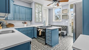 A kitchen with blue cabinets, a stove, and a ceiling fan. - The Darcy Victorian Home - Walk to Downtown, Grill, Large Dining (Hot Springs)