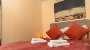 A neatly made bed with red and white pillows, a red blanket, and two white towels. - Warrington 3 (Double rooms) (Warrington)