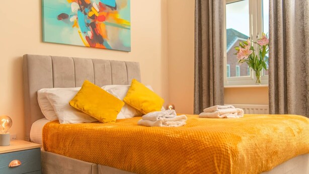 A neatly made bed with yellow and white pillows, a yellow blanket, and folded towels on a blue nightstand. - Warrington 5 (Double rooms) (Warrington)