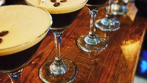 A bar with multiple glasses of a layered drink, possibly coffee-based, with a creamy top and coffee beans on the rim. - The Balavoulin (Aviemore)