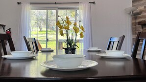 Una mesa de comedor con un tazón y un platillo blancos, dos sillas y una planta en maceta con flores amarillas.