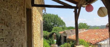A stone pathway leading to a rustic building with a wooden roof and a view of a red-tiled roofed area in the distance.