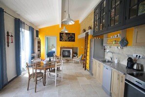 Een keuken met een eethoek, een open haard en een doorkijk naar een andere kamer.
