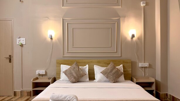 Une chambre d’hôtel avec un lit bien fait, deux tables de chevet et des lampes fixées au mur.