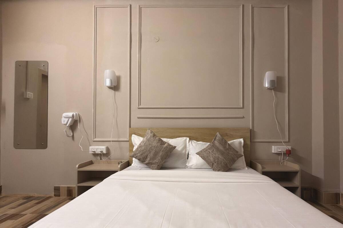 A hotel room with a large bed, two bedside tables, a mirror, and two wall-mounted lamps.