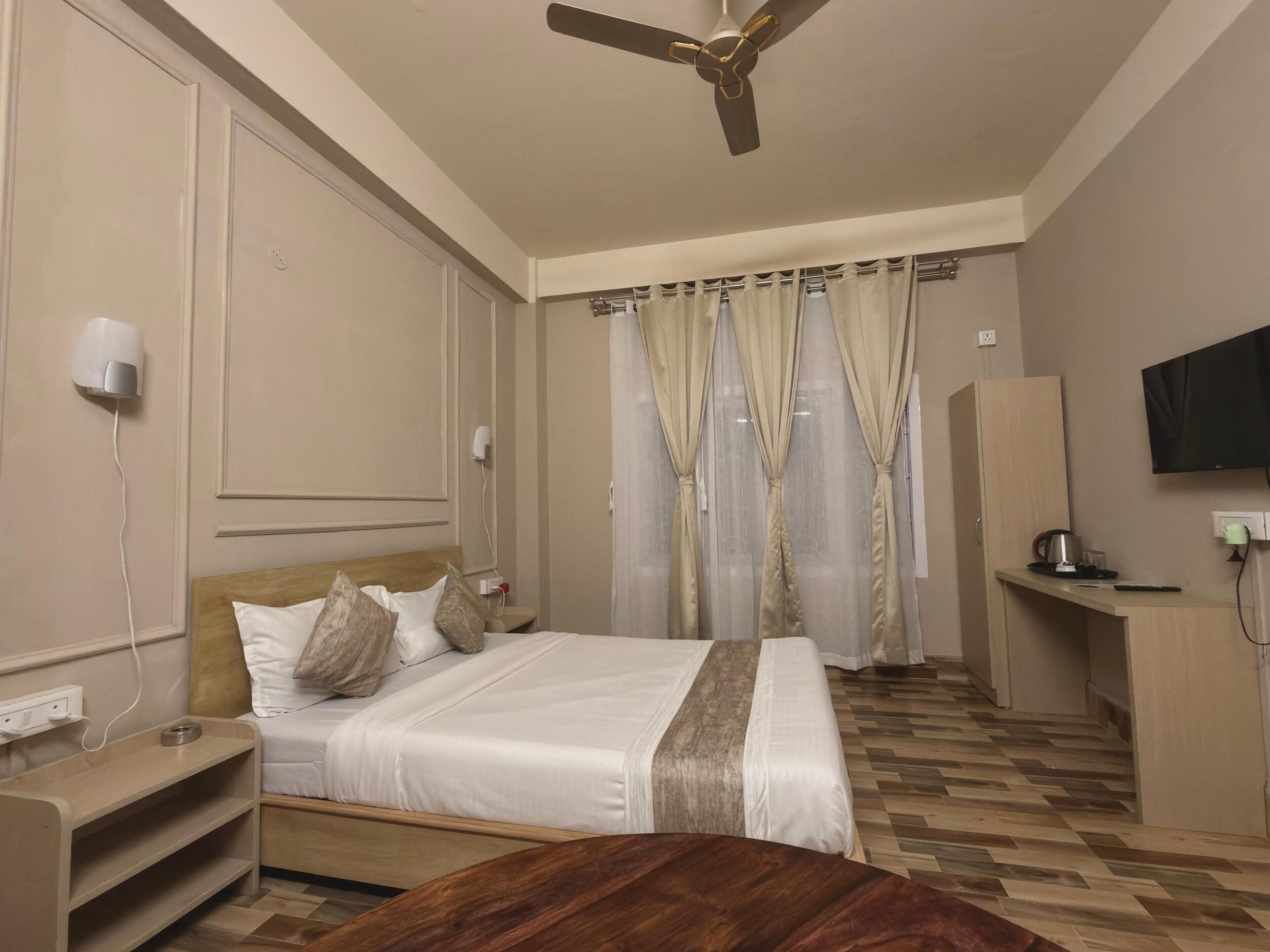 A hotel room with a bed, bedside table, TV, and a desk with a chair.