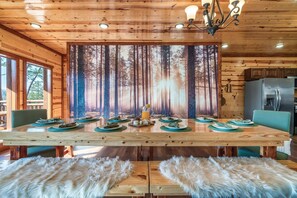 A wooden dining table with a forest-themed backdrop, surrounded by chairs and a fur-covered bench. - Incredible Family Cabin-Gamers Lounge & Theater Rm (Sevierville)