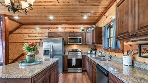 A modern kitchen with wooden cabinetry, granite countertops, stainless steel appliances, and a decorative welcome sign. - Incredible Family Cabin-Gamers Lounge & Theater Rm (Sevierville)