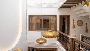 Un interior con varios niveles, lámparas doradas colgantes, una escalera y un balcón con barandillas.