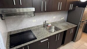 Eine moderne Küche mit dunklen Schränken, einer Granit Arbeitsplatte, einem eingebauten Herd und einer Edelstahl-Spüle.