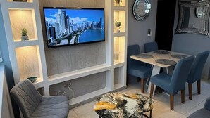 Ein modernes Wohnzimmer mit Flachbildfernseher, einem Esstisch mit Stühlen und einem Couchtisch.
