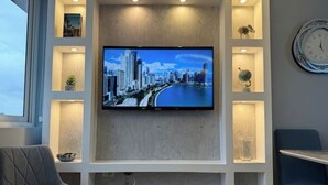 Ein modernes Wohnzimmer mit einem an der Wand befestigten Flachbildfernseher, einem grauen Sessel und einem kleinen Tisch.