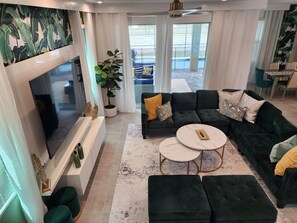 A modern living room with a large TV, dark green sofas, a white coffee table, and a potted plant. - Minutes from theme parks, Stunning House for 14+ guests (Kissimmee)