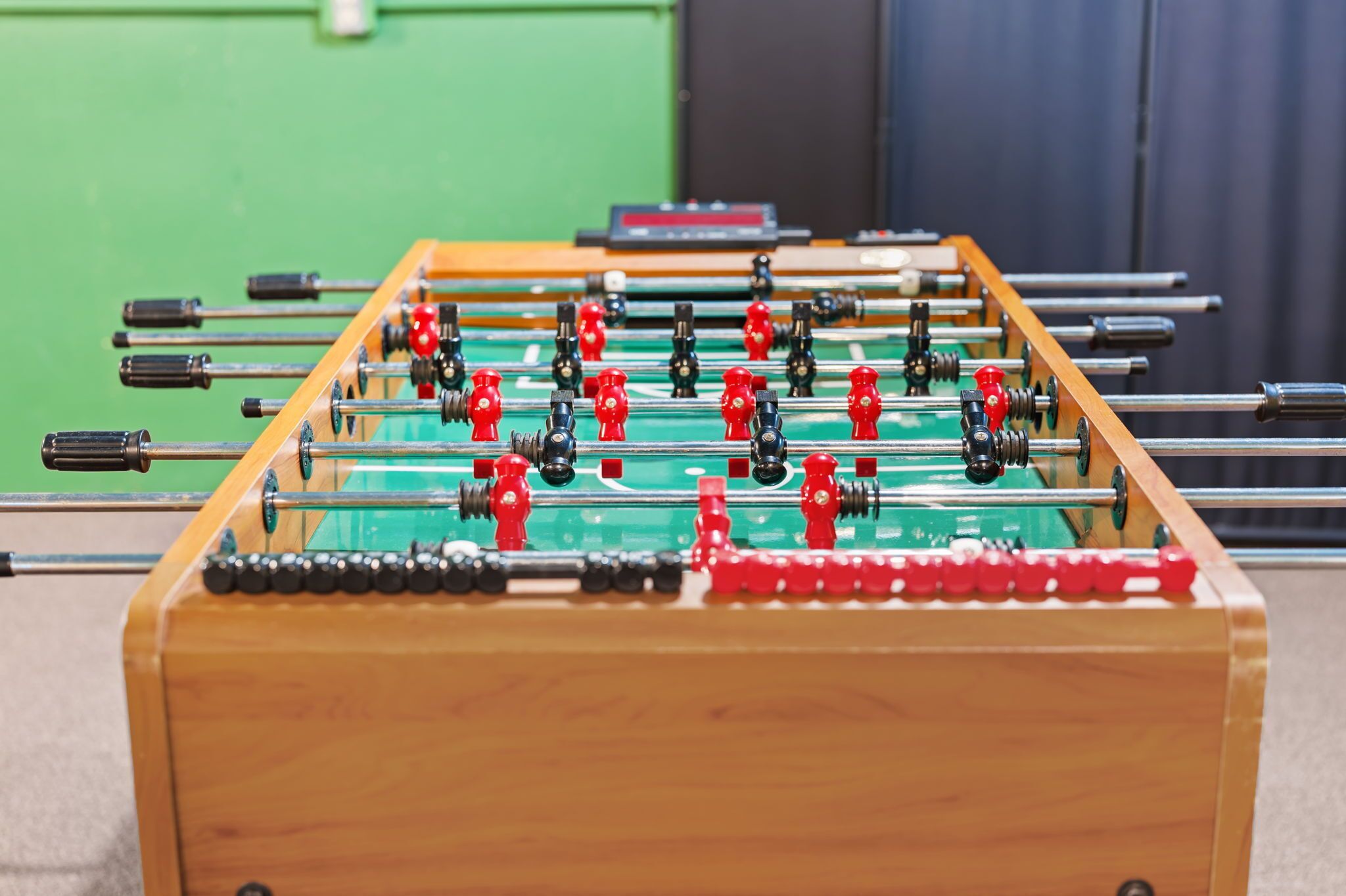 Une table de baby-foot avec des figurines rouges et noires, placée devant un mur vert.