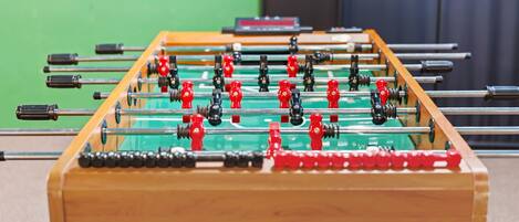 Une table de baby-foot avec des figurines rouges et noires, placée devant un mur vert.