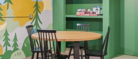 Una habitación con una mesa redonda de madera y cuatro sillas negras. En el fondo, una estantería verde con diversos objetos.