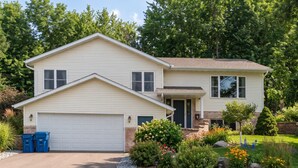 Ein zweistöckiges Haus mit Garage, Veranda und einem gepflegten Garten mit verschiedenen Pflanzen und Blumen.