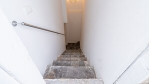 A narrow staircase with a metal handrail, a wall-mounted light fixture, and a door at the top.