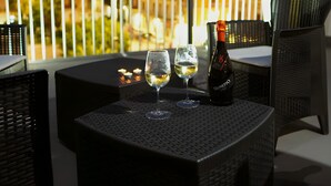 A balcony with wicker furniture, two wine glasses, and a bottle of wine.