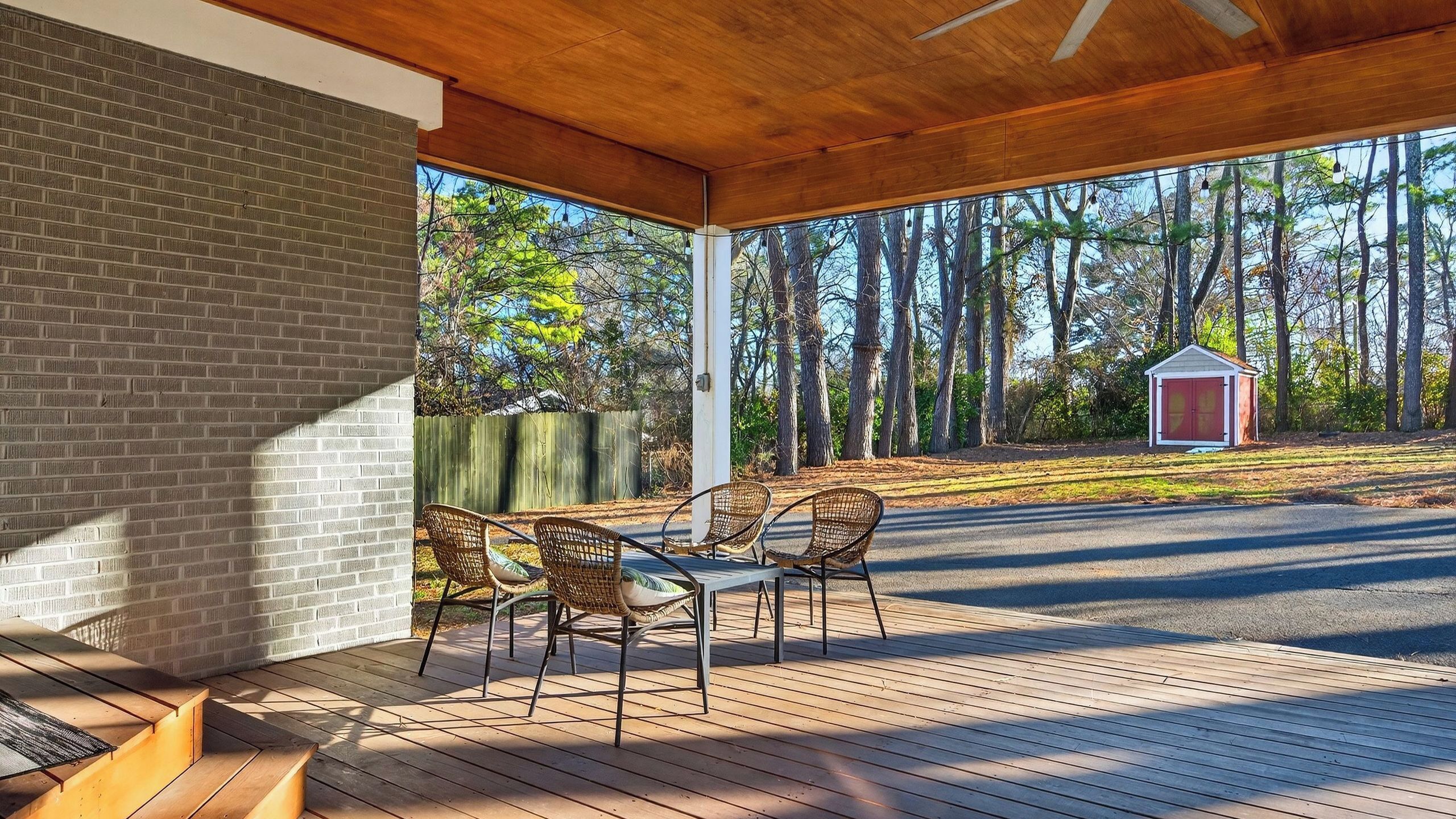 A covered outdoor patio with a brick wall, a table with chairs, and a view of a forest and a shed.