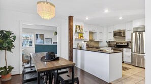 Eine moderne Küche mit weißen Schränken, einem Edelstahlkühlschrank und einem Holzespeisetisch mit einem Hut darauf.