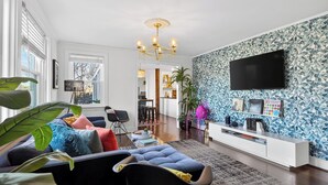 A modern living room with a sofa, a TV mounted on the wall, and a patterned wallpaper. - Historic Franklin Retreat Game Room Covered Patio Easy Downtown Access The Carolyn House by Avantstay (Franklin)